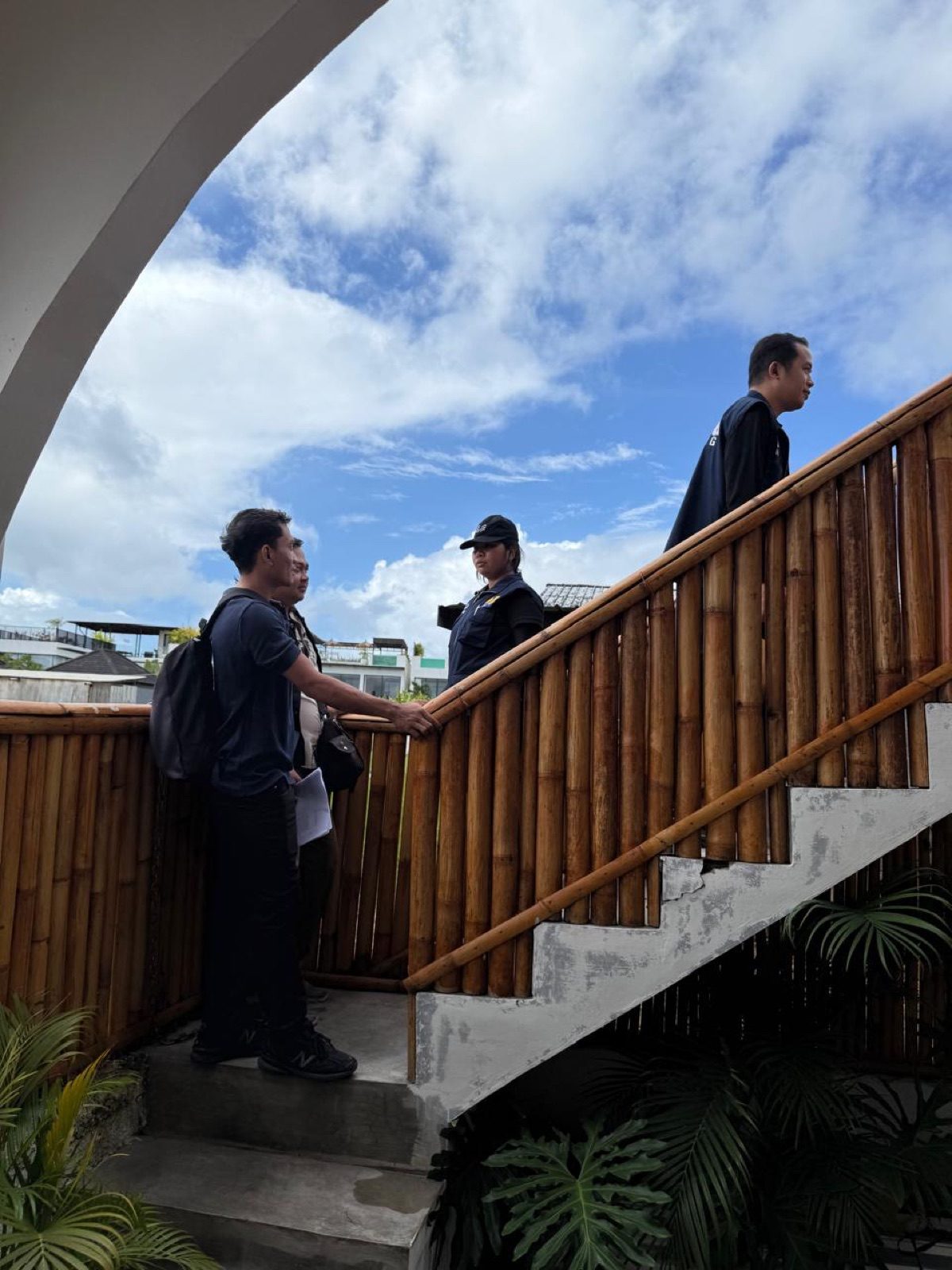 Siluet tim inspeksi menaiki tangga bambu bangunan komersial dengan latar langit biru dramatis